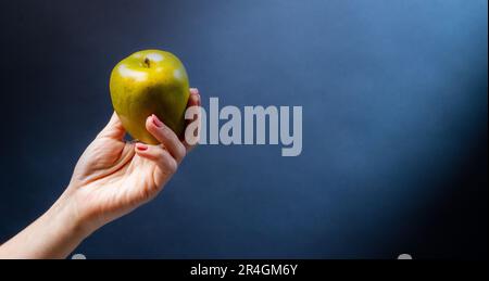 Hand holding green apple on blue background. Organic natural fresh fruit for vegan diet Stock Photo