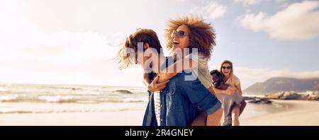 Happy couple enjoying a sunny day at the beach, with the man giving his girlfriend a piggyback ride. Young lovers having a romantic summer vacation, m Stock Photo