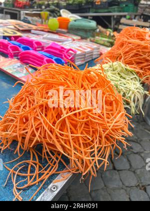 vegetables, pile or heap of grated carrot and raw vegetables in noodle shape on counter of open farmers market with selective focus. thin grated carro Stock Photo
