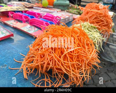 vegetables, pile or heap of grated carrot and raw vegetables in noodle shape on counter of open farmers market with selective focus. thin grated carro Stock Photo