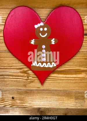Heart, hand drawn gingerbread cookie shape on red heart hanged on wooden background or surface with copy space Stock Photo