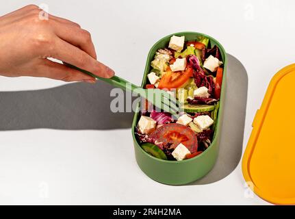 Hand with fork eating healthy salad in plastic lunch box. Vegetable mix inside lunchbox. Stock Photo