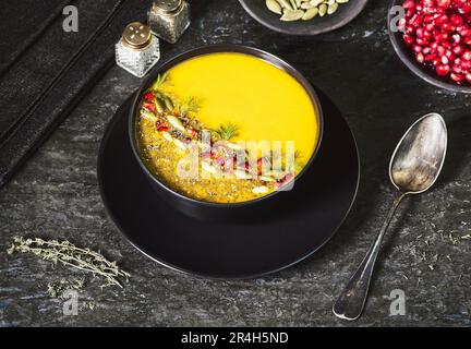 Pumpkin and carrot soup decorated with pomegranate arils, chia seeds, crunchy pumpkin seeds, chopped dill and a sprinkle of ground black pepper. Stock Photo