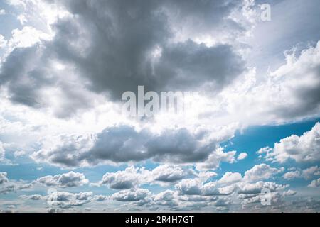 A dynamic wide angle cloudscape featuring thick gray cumulus clouds contrasting against a vibrant blue sky during daytime weather Stock Photo