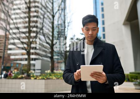 Young Asian business man professional standing in city using digital tablet. Stock Photo