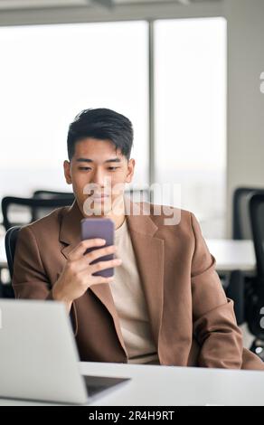 Young busy Asian business man using smartphone in office. Vertical Stock Photo