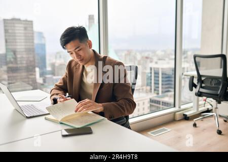 Busy young Asian business man working in office checking notebook. Stock Photo