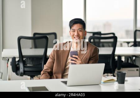 Young happy smiling Asian business man using cell phone in office. Stock Photo