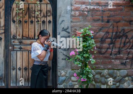 bonita chica indigena aprendiendo fotografia en la calle, sacando fotografia a una planta con flores Stock Photo