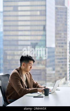 Young serious busy Asian business man typing on laptop using computer in office. Stock Photo