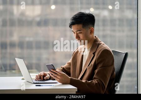 Young serious busy Asian Japanese business man using phone in office. Stock Photo