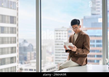 Young Asian business man executive using tablet sitting in modern office. Stock Photo