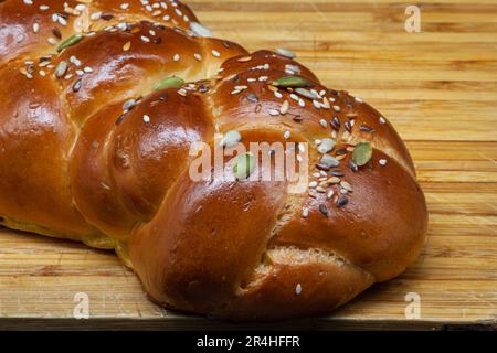 A white challah loaf on a wooden board with linseeds, sunflower seeds and pumpkin seeds. Golden freshly baked crust with highlights. Stock Photo