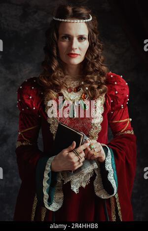 medieval queen in red dress with book and handkerchief on dark gray background. Stock Photo
