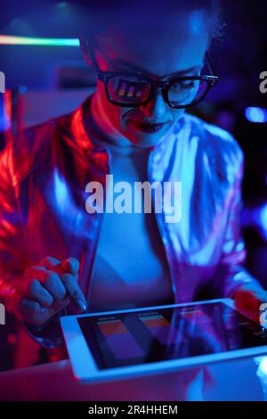 Neon metaverse futuristic concept. trendy female in glasses with tablet PC and charts reflecting in glasses in modern office. Stock Photo
