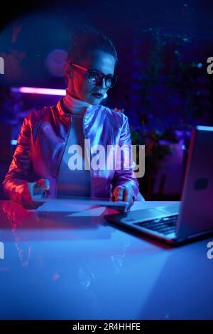 Neon metaverse futuristic concept. elegant female in glasses with laptop using tablet PC in modern office. Stock Photo