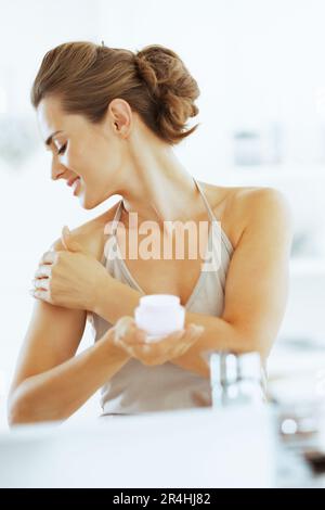 Happy young woman applying cream in bathroom Stock Photo