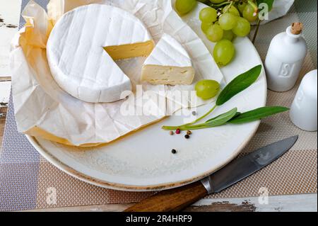 Camembert soft cheese on the plate with grapes and herbs Stock Photo
