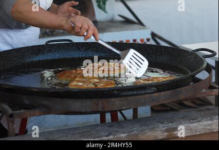 Cook woman roasts flour pastries in a large pan with butter outdoor Stock Photo