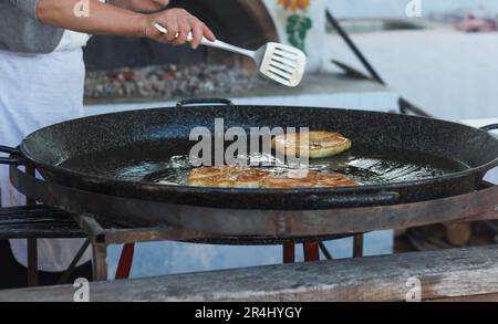 Cook female roasts flour pastries in a large pan with butter outdoor Stock Photo