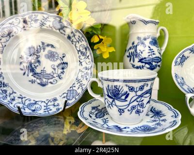 Porcelain tea cup and plates on window display of a china shop with selective focus and street reflection. porcelain cup, mug and plates with blue flo Stock Photo