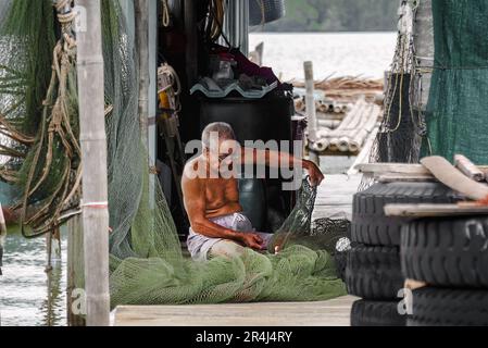 Chantaburi, Thailand, March 21, 2023: An old man mends the fishing net inside his pontoon hut. Stock Photo