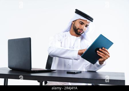 Emirate middle-eastern businessman wearing kandora working in the office, Dubai - Handsome corporate business man sitting at computer desk and remote Stock Photo