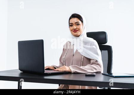 Beautiful arab middle-eastern corporate businesswoman with traditional abaya dress working in the office- Arabic muslim adult female portrait at compu Stock Photo