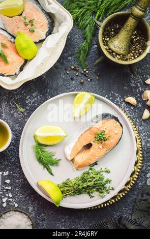 Fresh raw salmon steak placed with lemon, garlic, salt and mixed pepper, olive oil, organic oregano and dill. Top view with close-up. Stock Photo