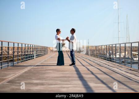 Loving Senior Couple Standing Holding Hands At Marina Pier Outside Stock Photo