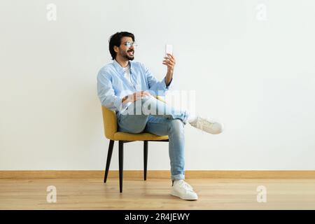 Cheerful millennial middle eastern guy blogger in glasses has video call, shooting blog on smartphone Stock Photo