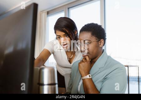 Female programmer discussing with colleague over computer in office Stock Photo