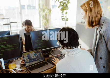 Manager discussing with programmer over computer at desk in office Stock Photo