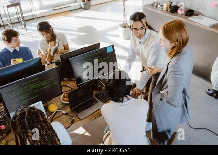 Businesswoman discussing with male and female programmers at desk in startup office Stock Photo