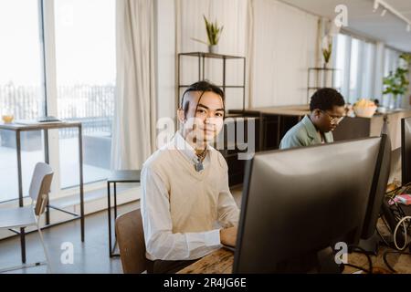 Portrait of hipster young male programmer sitting at computer desk in office Stock Photo