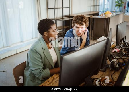 Multiracial programmers discussing over computer at desk in creative office Stock Photo