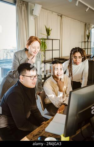 Multiracial male and female programmers discussing over computer at desk in creative office Stock Photo
