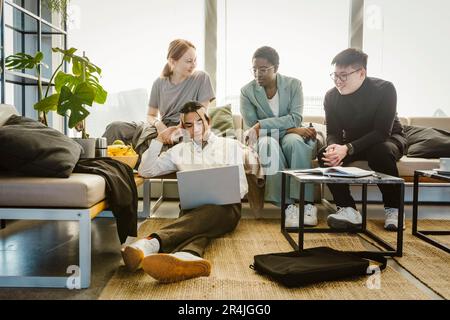 Multiracial male and female colleagues discussing over laptop in creative office Stock Photo