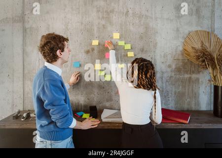 Male and female colleagues discussing over adhesive notes on wall in creative office Stock Photo