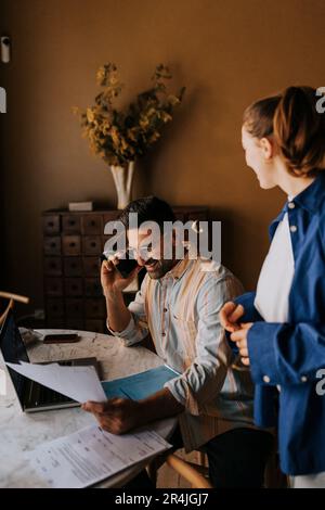 Happy man talking on smart phone by non-binary person at home Stock Photo
