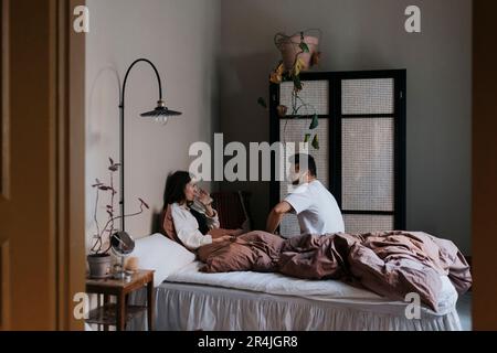 Couple talking to each other while sitting on bed at home Stock Photo