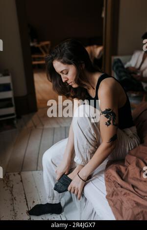 Non-binary person wearing sock while sitting on bed at home Stock Photo