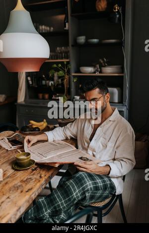 Man reading newspaper while sitting on chair at home Stock Photo