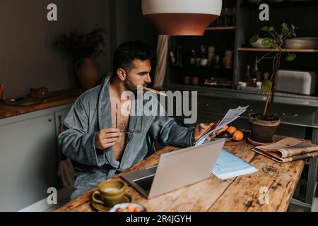 Man using smart phone while holding financial bills at dining table Stock Photo