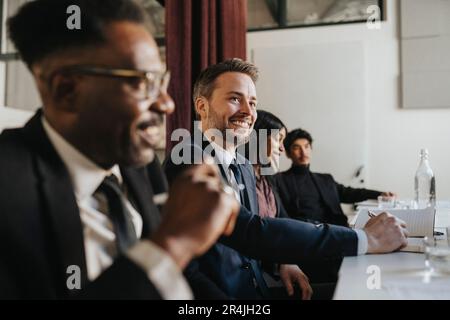 Smiling businessman looking away while sitting with colleagues during meeting at office Stock Photo