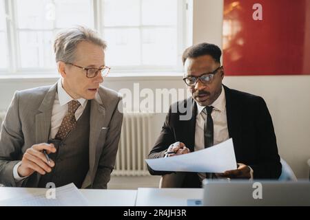 Male entrepreneurs discussing over document sitting in board room at office Stock Photo