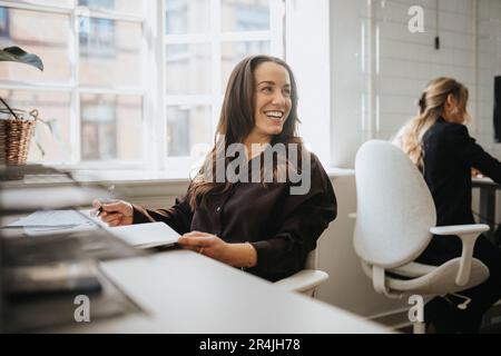 Happy female entrepreneur looking away while sitting at desk in office Stock Photo