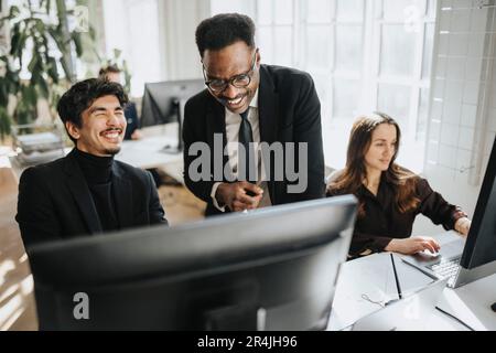 Happy male colleagues discussing over computer at office Stock Photo