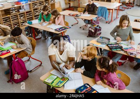 Teacher explaining male and female students sitting in classroom Stock Photo