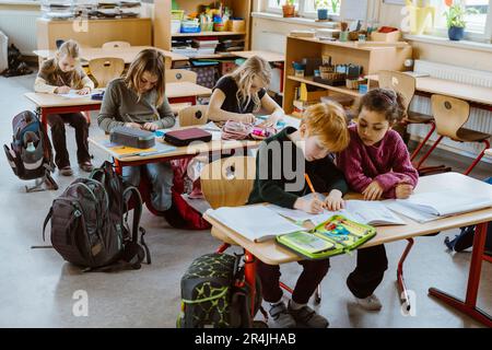 Male and female students studying together sitting at desk in classroom Stock Photo